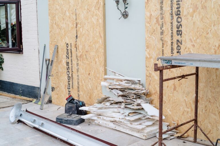 A contractor inspects a stack of reclaimed wood beams and bricks at a residential construction site.