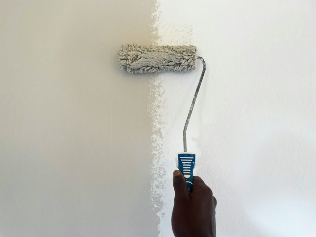 A homeowner reads a low-VOC paint label beside an open window and ventilation fan.