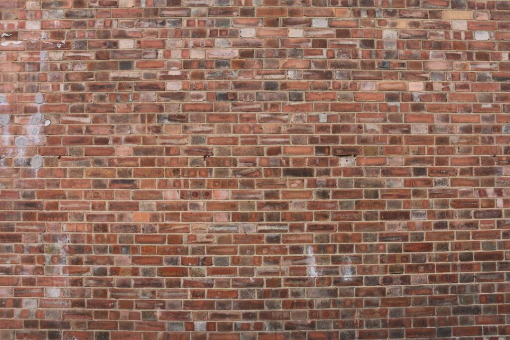 A mason compares mortar samples beside weathered brick joints on an older masonry wall.