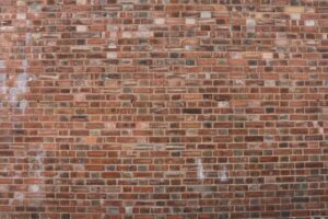 A mason compares mortar samples beside weathered brick joints on an older masonry wall.