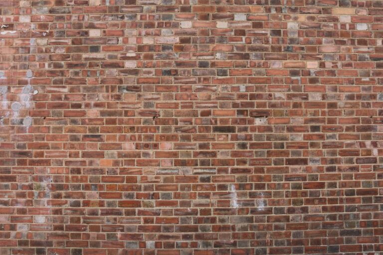 A mason compares mortar samples beside weathered brick joints on an older masonry wall.